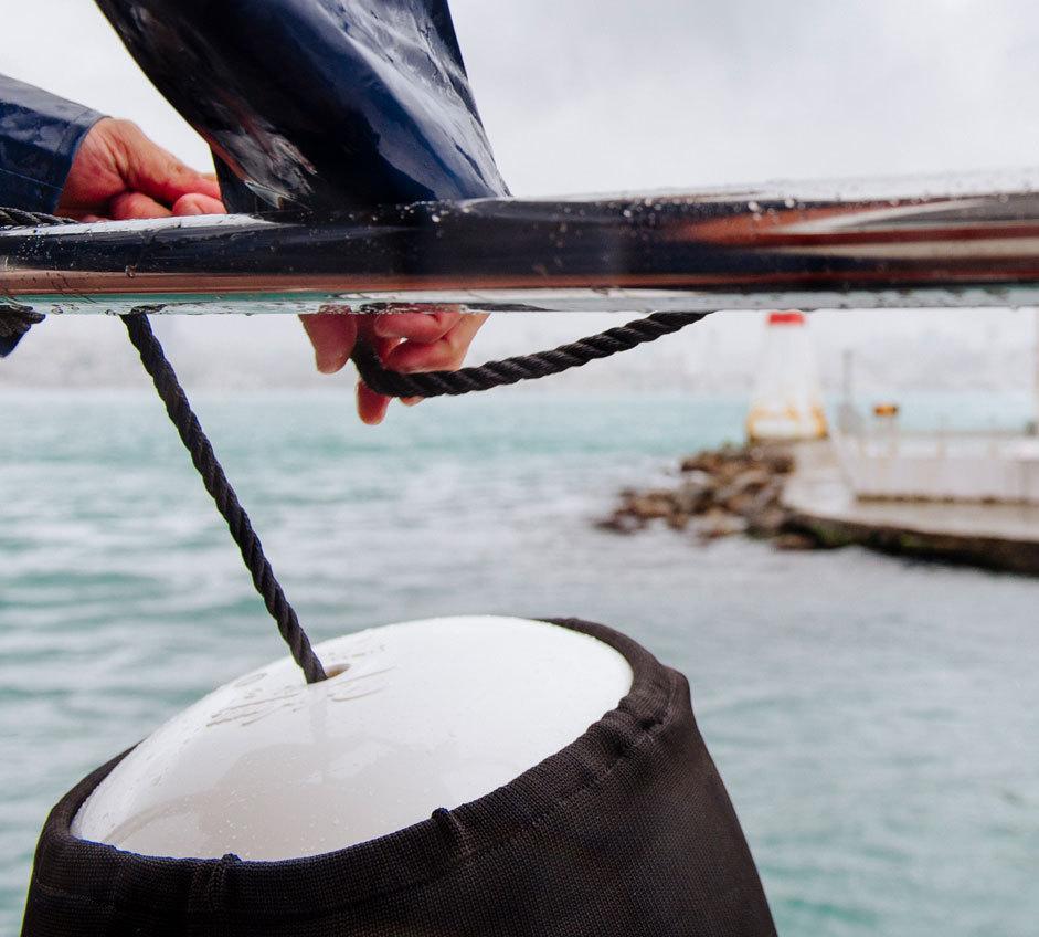 Hands on boat rail holding rope fender line attached to boat fender in cover, Turkey