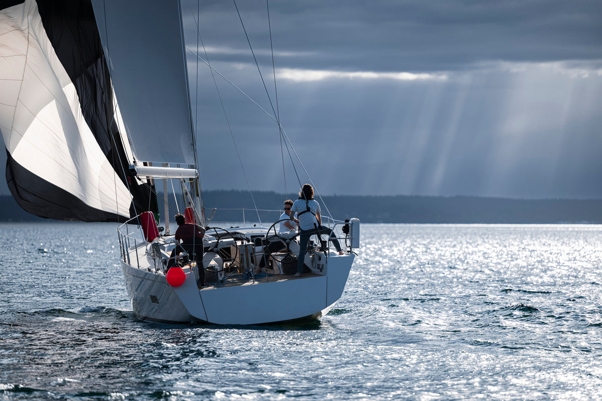 sailing boat with red Polyform US A-Series buoy, with crew in the Pacific Northwest with stormy sky in the background