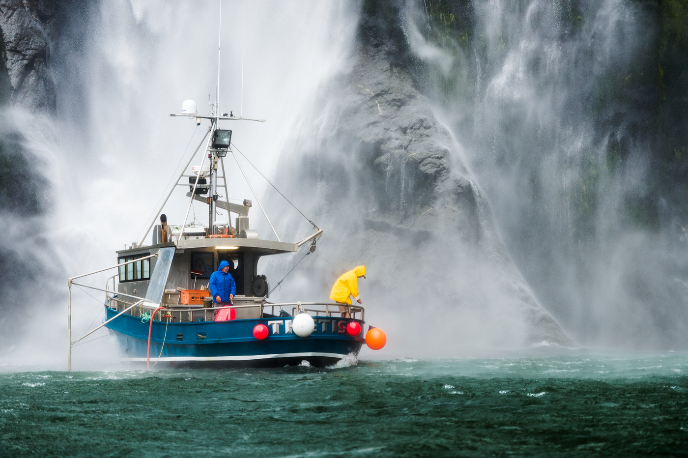 Boat fenders and buoys in use on fishing boat with crew near waterfall in New Zealand
