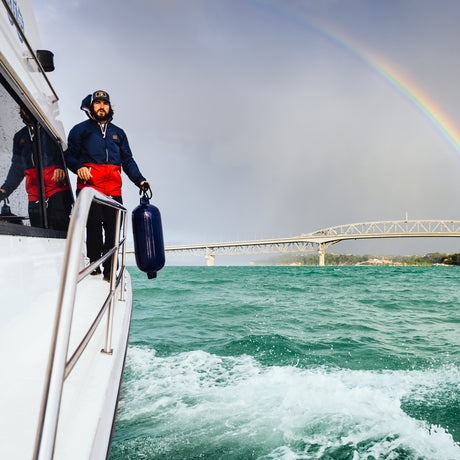 Boat fender held by man walking on deck of boat in New Zealand with rainbow in sky over bridge